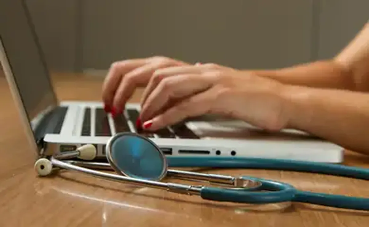 Médica digita no computador, tendo seu estetoscópio ao lado. Foto: National Cancer Institute/Unsplash