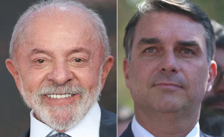 Dois homens aparecem em retratos lado a lado. O da esquerda é um homem mais velho, com cabelo grisalho e barba branca, sorrindo, vestido com terno escuro, camisa branca e gravata azul. O da direita é um homem mais jovem, com cabelo escuro penteado para o lado, expressão neutra, vestindo terno escuro