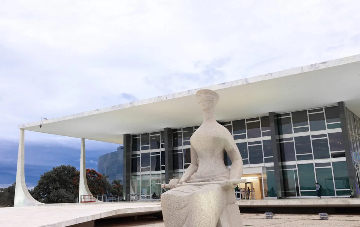 Foto em formato paisagem do prédio do STF com a Estátua da Justiça em primeiro plano